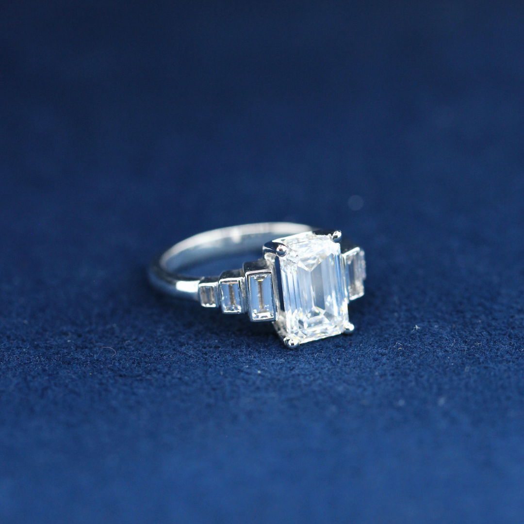 A left-side view of a fine jewelry emerald-cut moissanite diamond ring in 925 sterling silver, showcasing the sleek band and the radiant center stone.