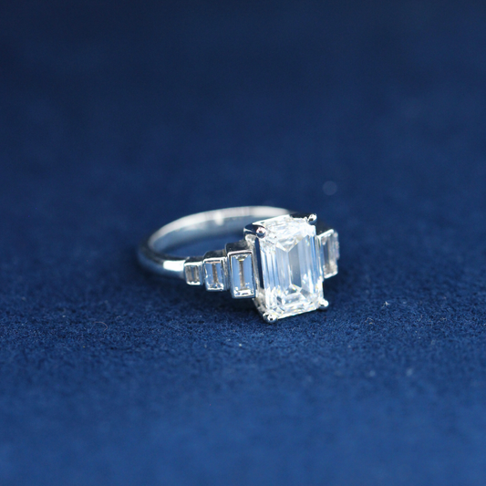 A left-side view of a fine jewelry emerald-cut moissanite diamond ring in 925 sterling silver, showcasing the sleek band and the radiant center stone.